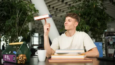 A pupil sits at a desk learning and spins a book on his finger.
