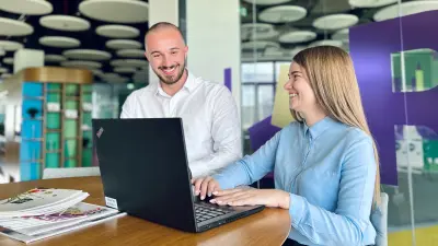 Two graduates are talking at a high table and looking into a laptop.