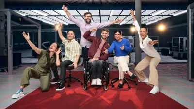 Six people can be seen on a red carpet in a lab. They cheer, laugh and strike various poses.