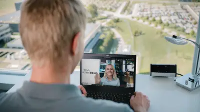 The testimonial Joachim can be seen from behind. He is sitting in front of a window at a table on which there is a desk lamp and a laptop. A woman can be seen on the laptop screen talking to him through the laptop.